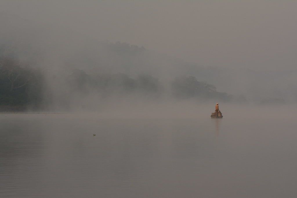A boat navigates the calm, mist-shrouded waters of the Rapti River in Chitwan National Park.