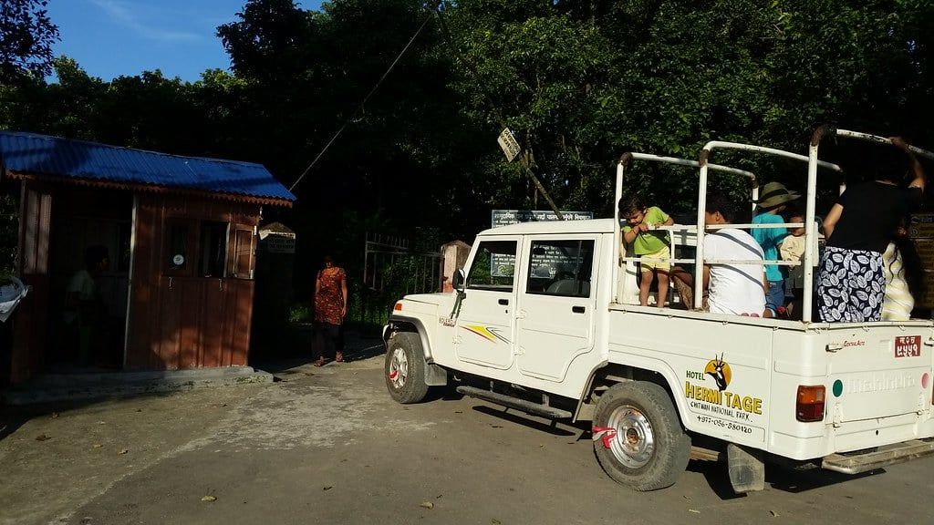 Visitors seated in an open-backed safari jeep parked near an entrance booth in Chitwan National Park.